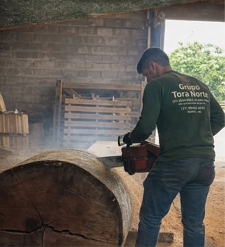 Funcionário da Tora Norte cortando uma tora grossa com motosserra no pátio
